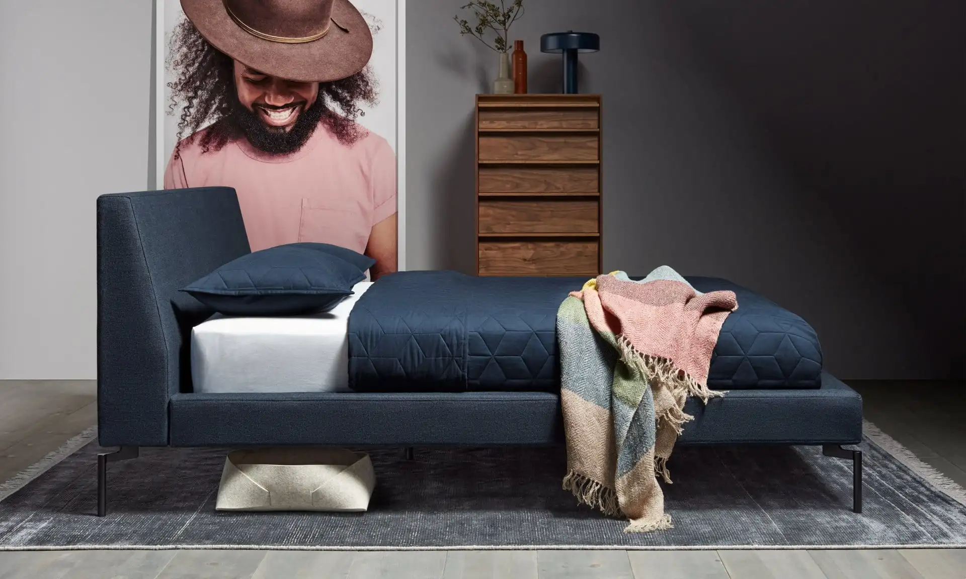 Modern navy bed in small men's bedroom with geometric quilt.