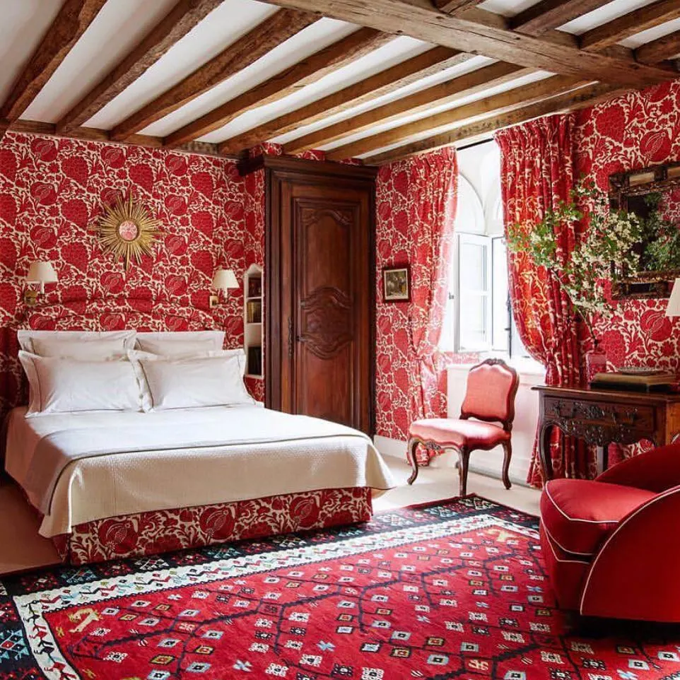 Rustic red bedroom with floral wallpaper and exposed beams.