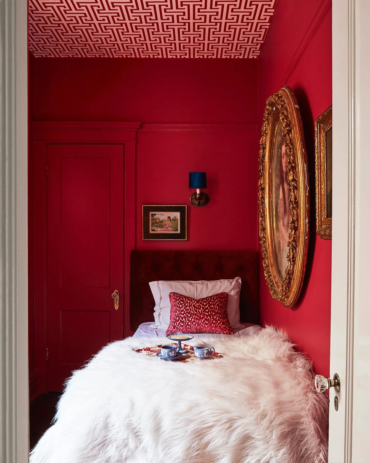 Small red bedroom with geometric ceiling wallpaper.