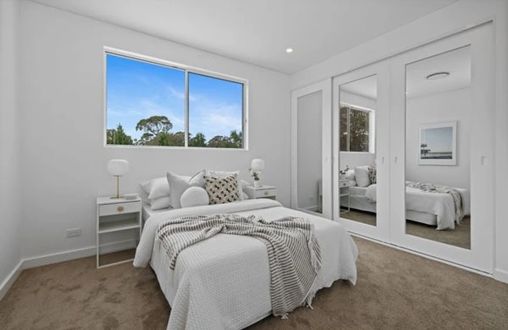Small bedroom with mirrored closet doors and white decor.