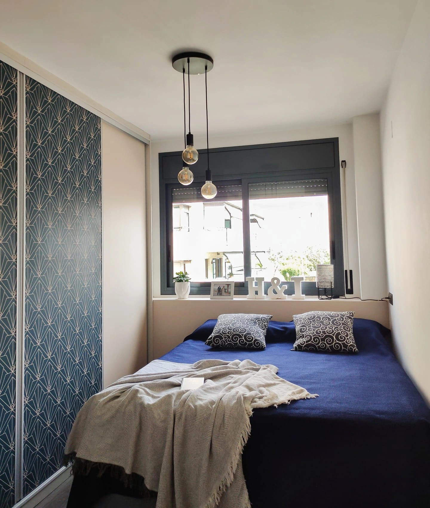 Small bedroom with a navy blue bed, a patterned closet, and modern pendant lights.