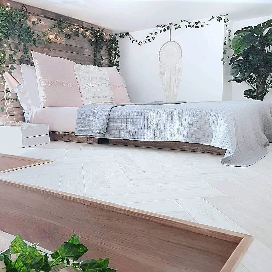 Bohemian bedroom with a wood pallet bed, fairy lights, and green plants.
