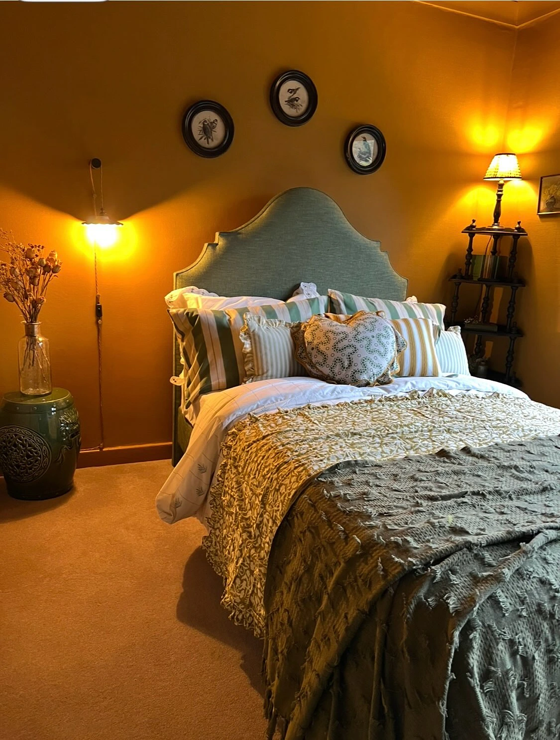 Green headboard with warm golden walls and layered bedding.  