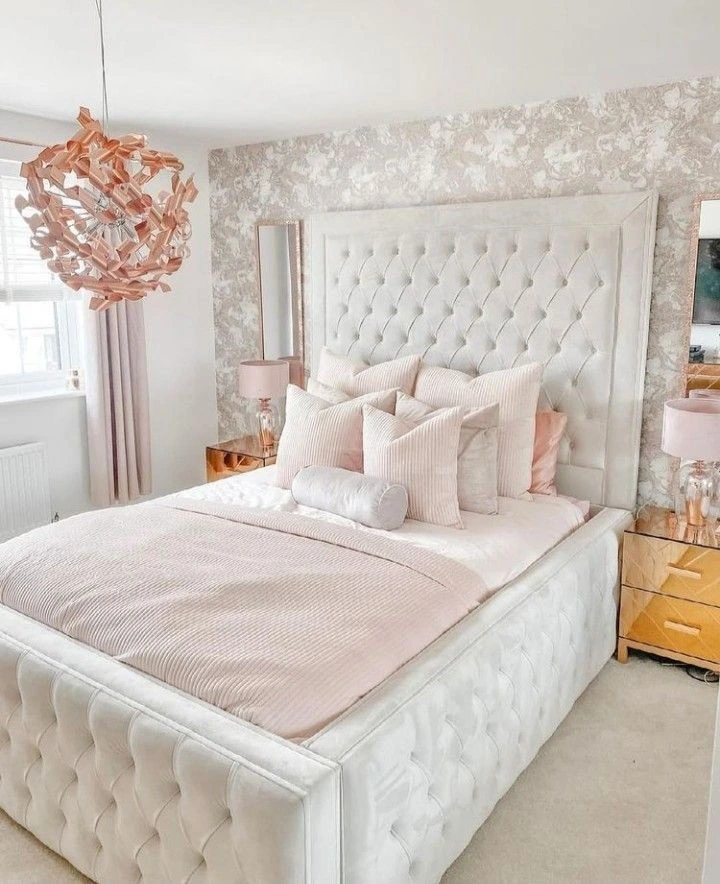 Blush tufted bed and gold accents in small bedroom.