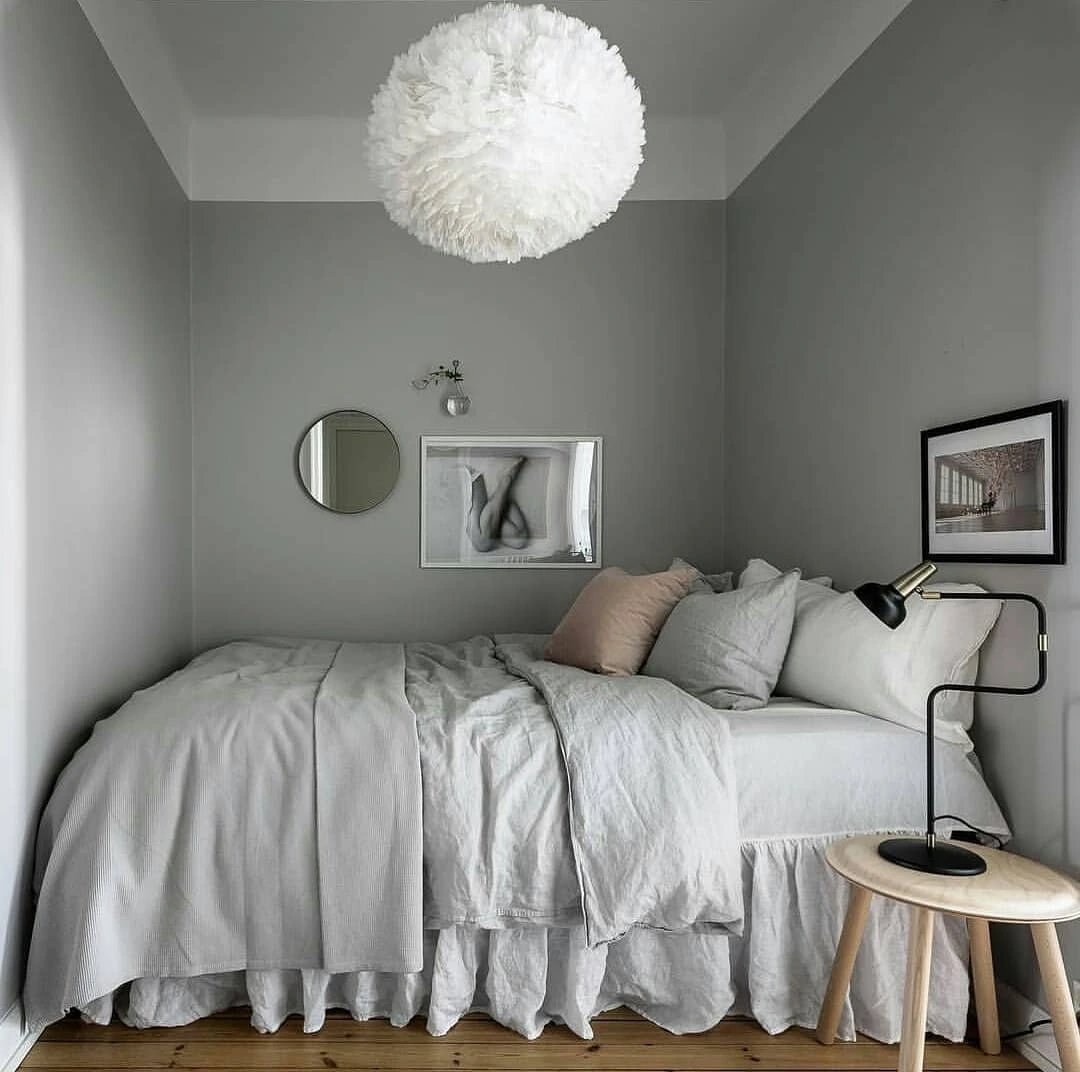 Gray minimalist bedroom with feathery pendant light and wooden stool.